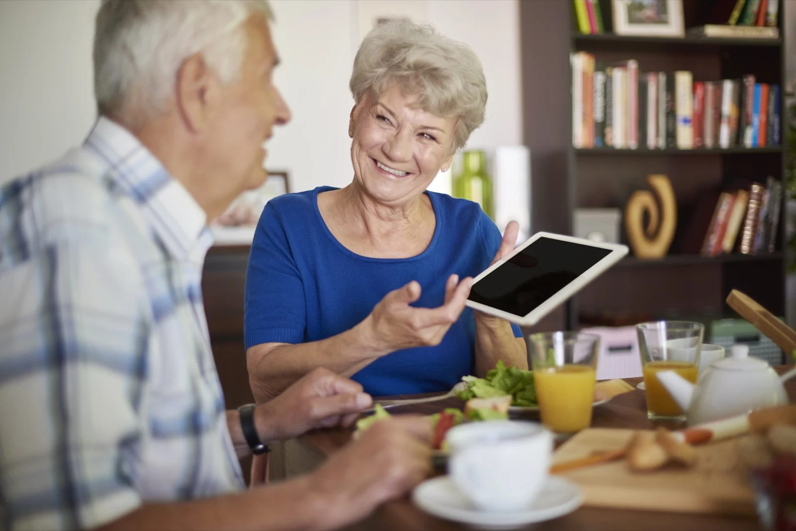 Un couple de seniors souriant avec une tablette et des jus de fruits frais