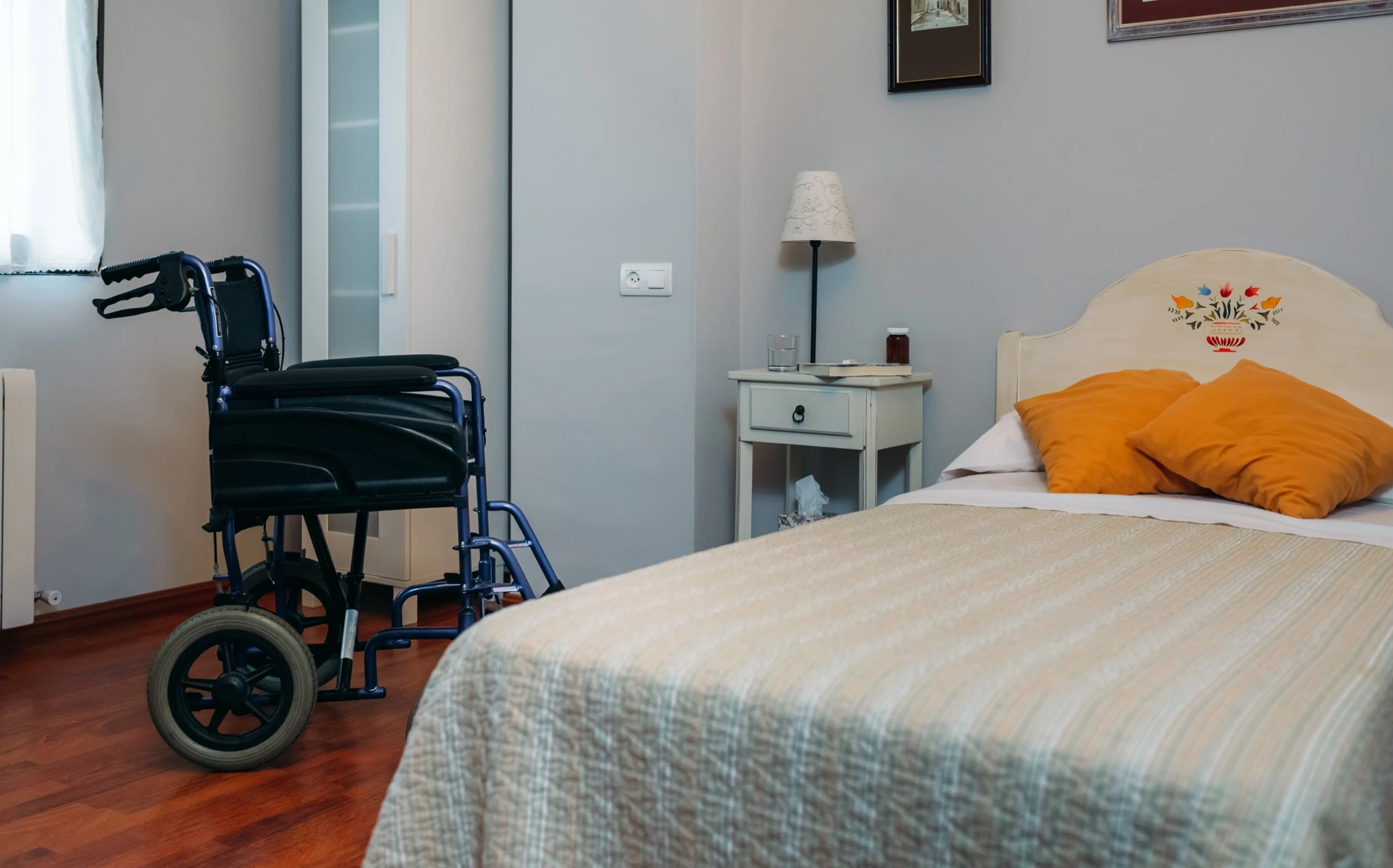 Chambre d'EHPAD chaleureuse meublée avec fauteuil personnel, lit médicalisé et fauteuil roulant, espace privatif accueillant et personnalisable