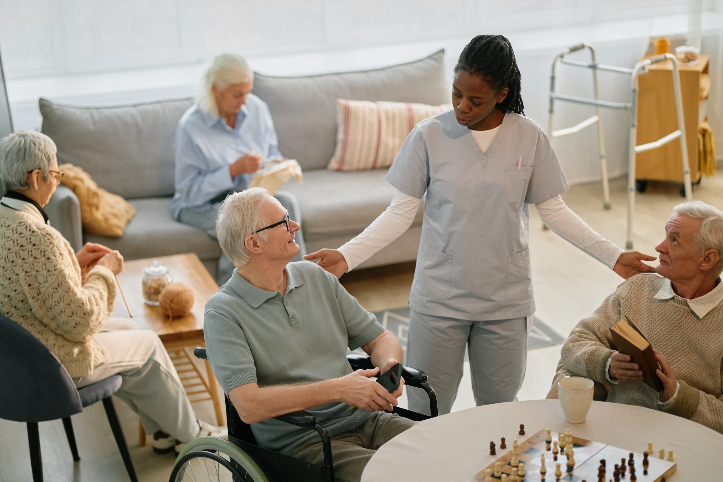 Soignante EHPAD interagit avec plusieurs résidents seniors dans la salle commune, ambiance chaleureuse et lien humain au quotidien