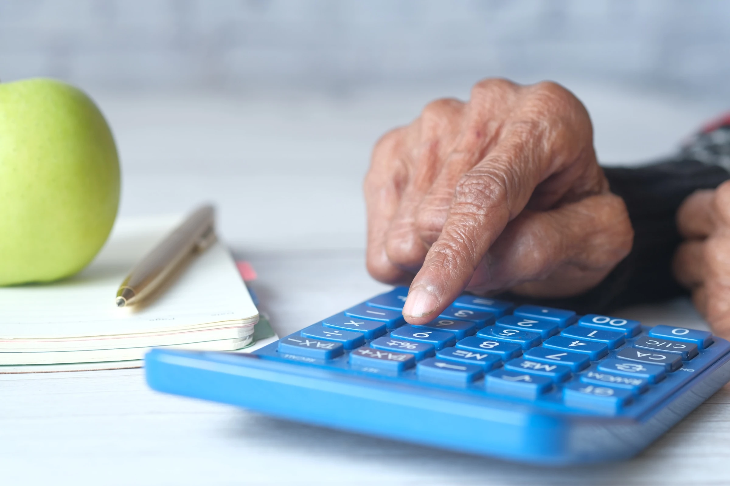 Femme senior utilisant une calculatrice à son bureau pour estimer le coût mensuel d'une chambre en unité protégée, calcul du reste à charge et aides