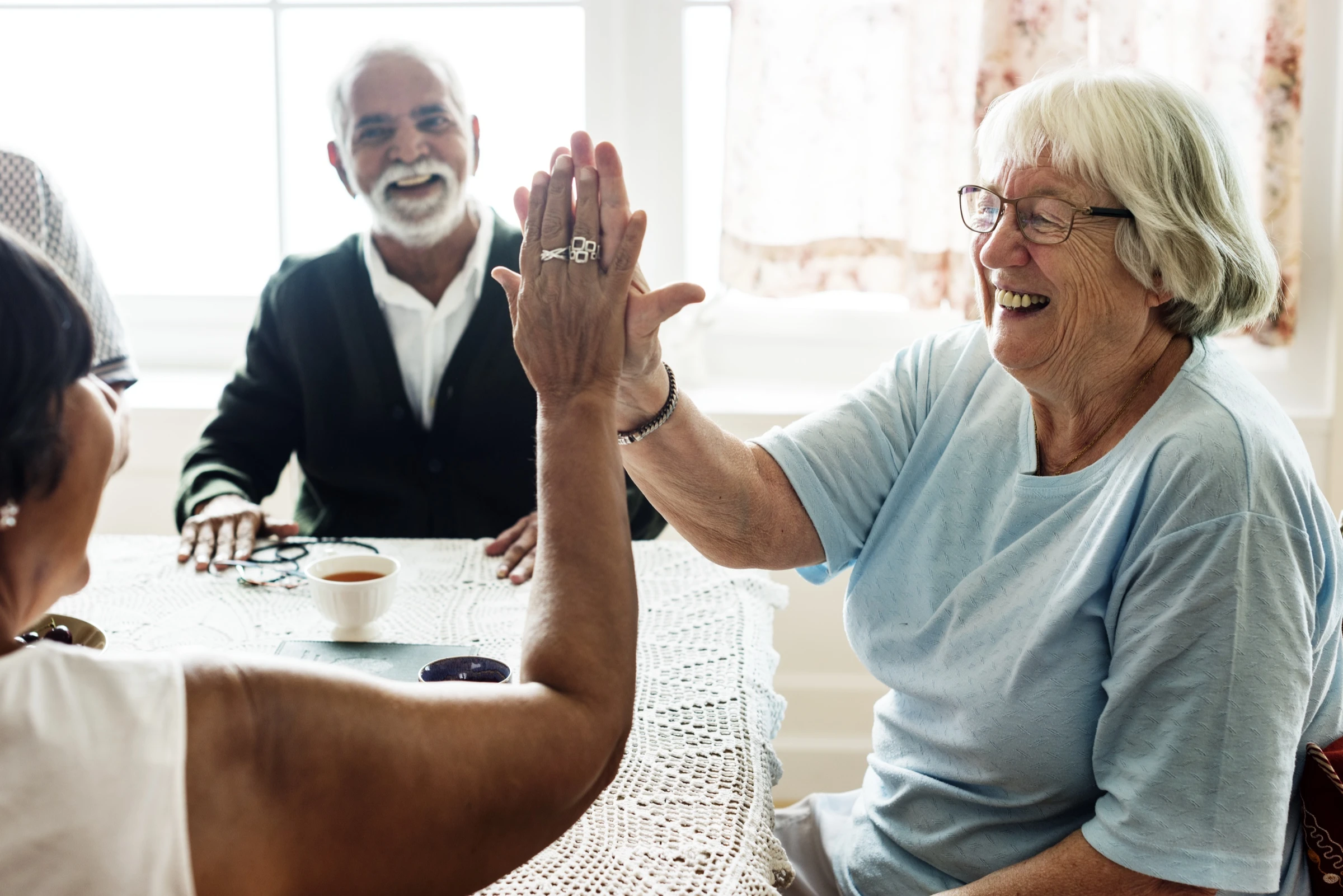 Deux femmes seniors se tapent dans la main avec complicité et joie en EHPAD, vie sociale active et lien préservé entre résidents GIR 2 et GIR 3