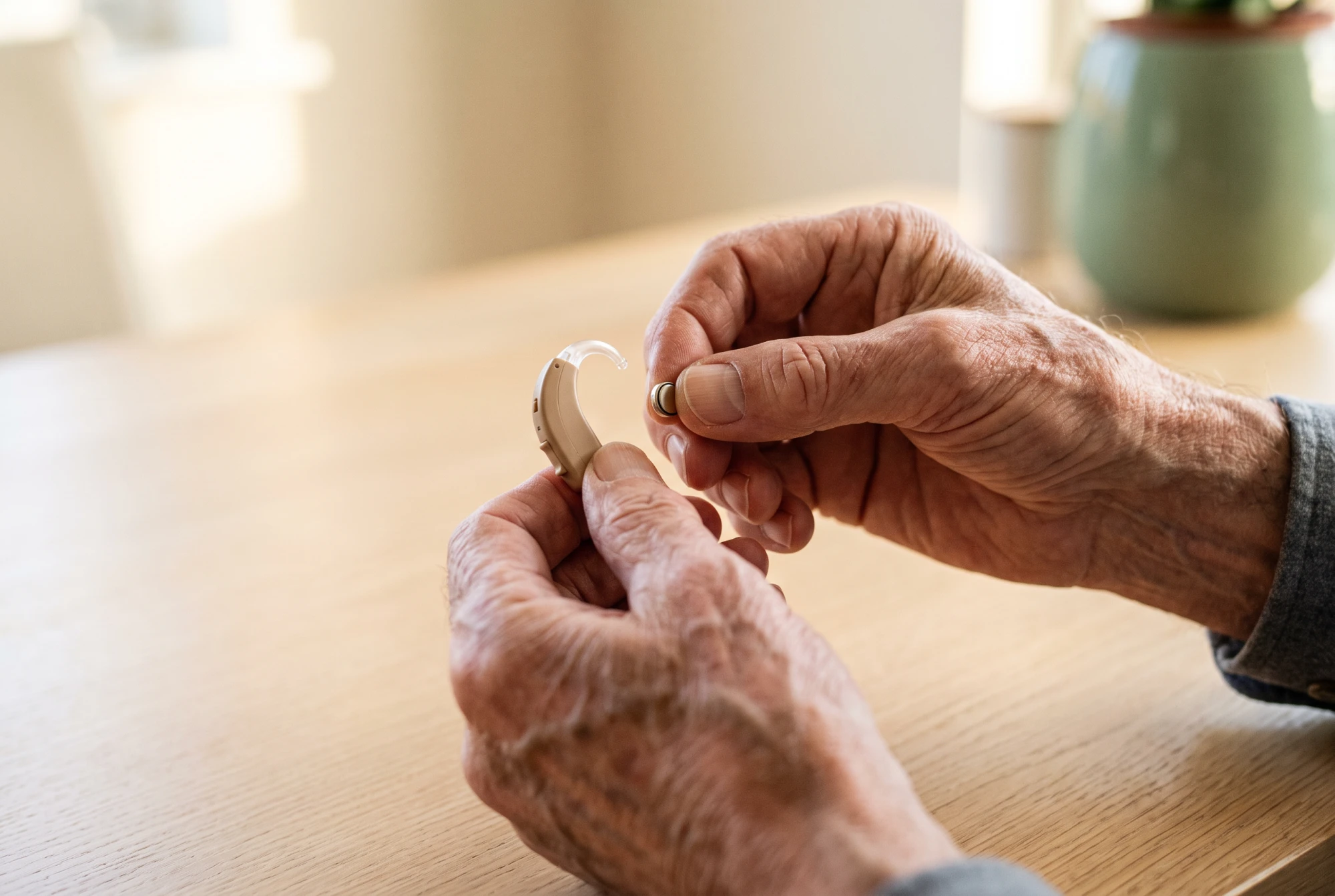 Mains d'un homme âgé manipulant un petit appareil auditif contour d'oreille et sa pile minuscule.