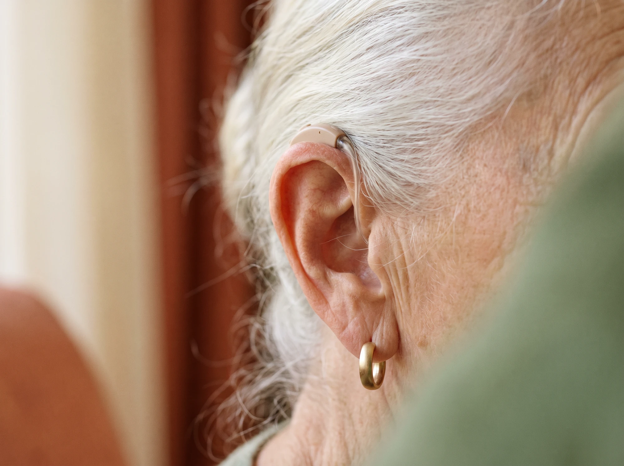 Gros plan sur un petit appareil auditif contour d'oreille discret porté par une femme âgée aux cheveux blancs.