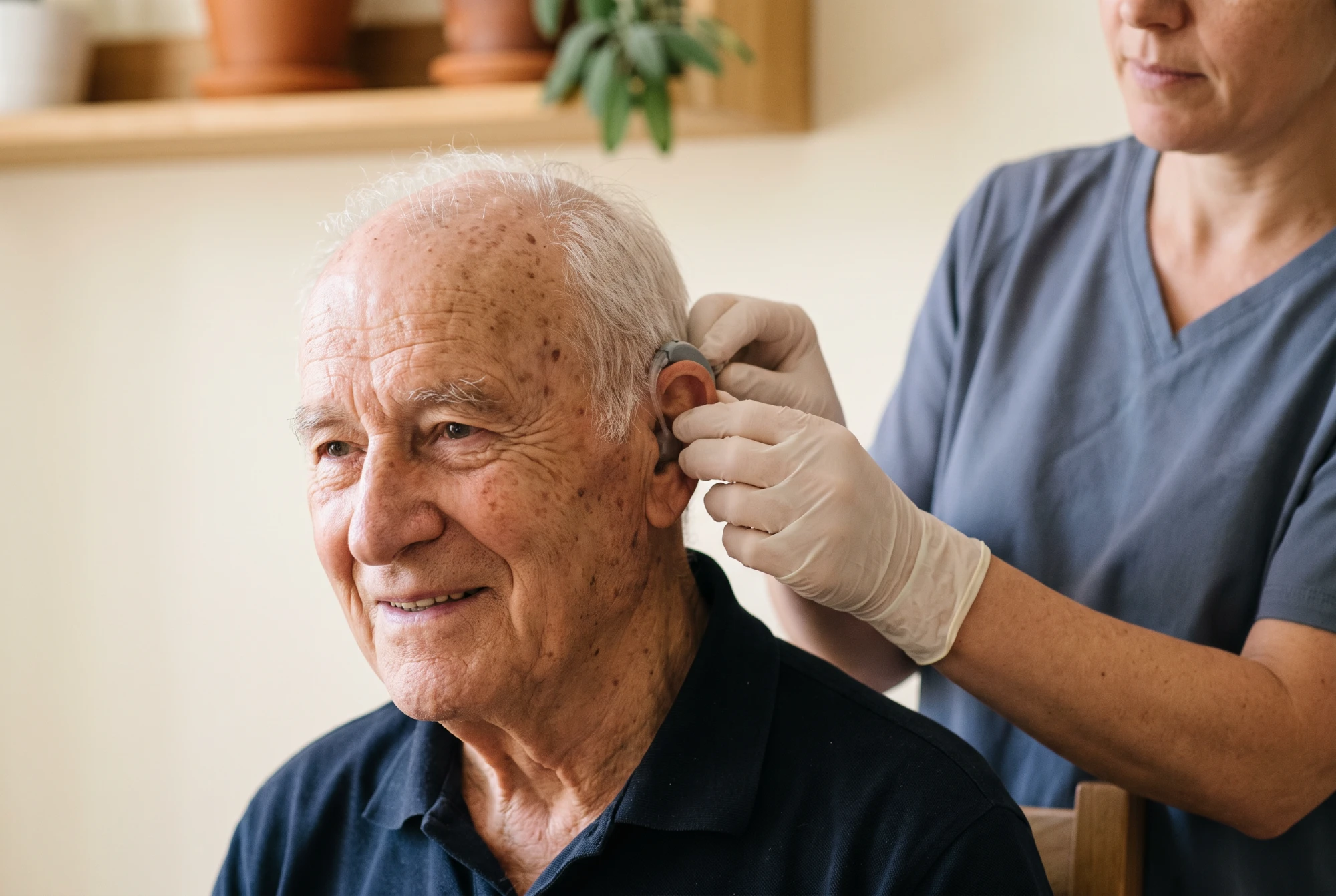 Audioprothésiste réglant un appareil auditif sur l'oreille d'un homme âgé souriant en cabinet clair