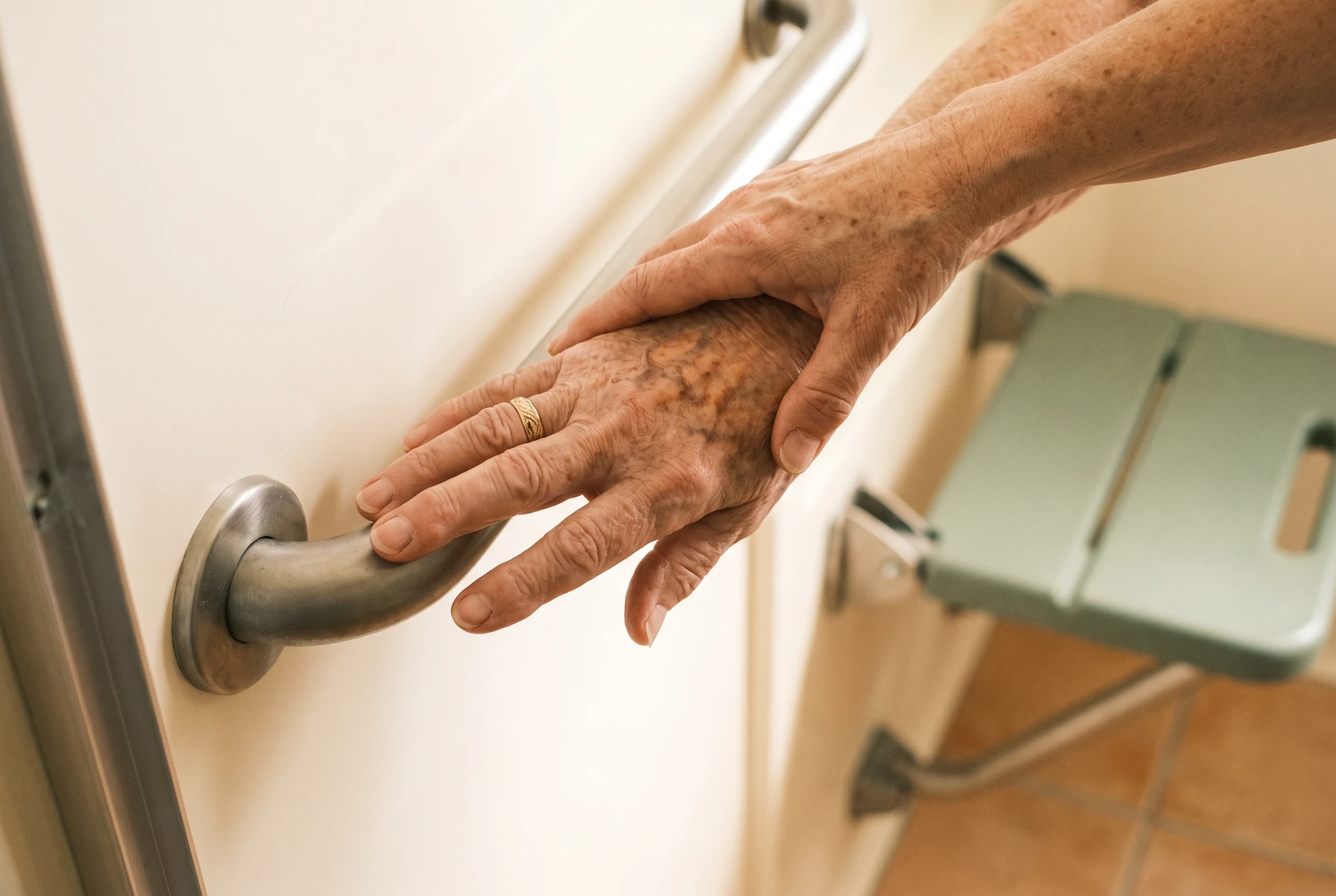 Main d'une fille aidante guidant celle de sa mère âgée vers la barre d'appui d'une douche senior sécurisée.