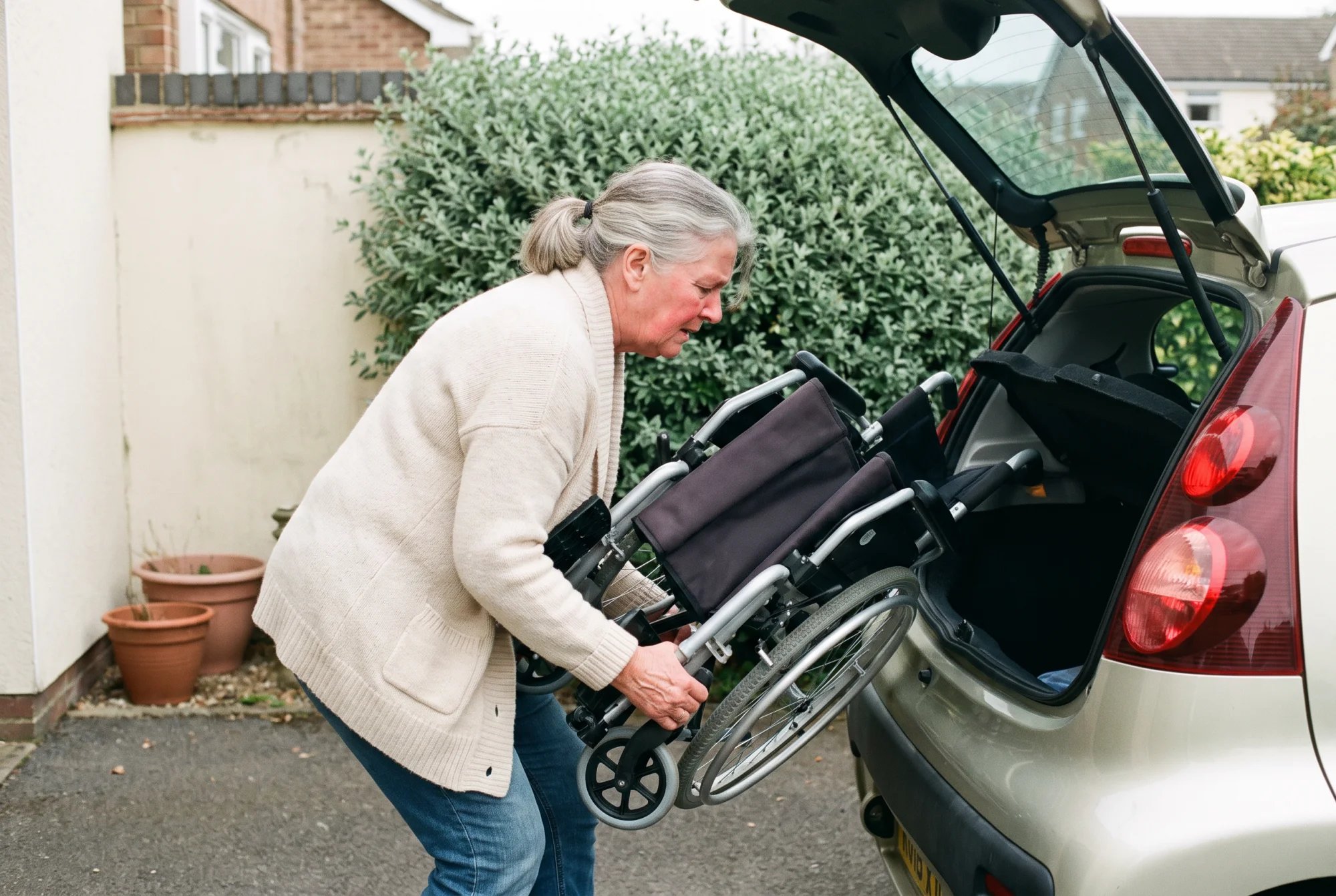 Aidante de 60 ans pliant seule un fauteuil de transfert léger pour le charger dans le coffre de sa voiture.