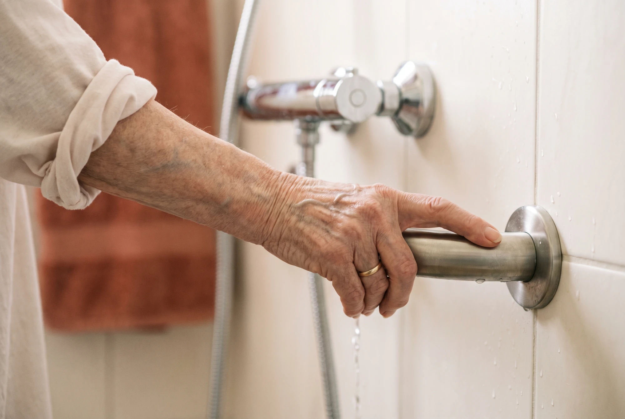 Main ridée d'une femme âgée agrippant une barre d'appui horizontale en inox dans une douche de plain-pied.